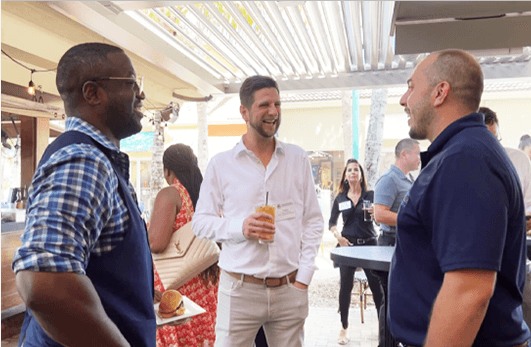 Three individuals chatting with drinks in hand at a networking event