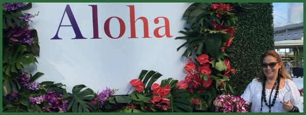 CEO of Paragon Events pointing to white Aloha sign, surrounded by tropical flowers