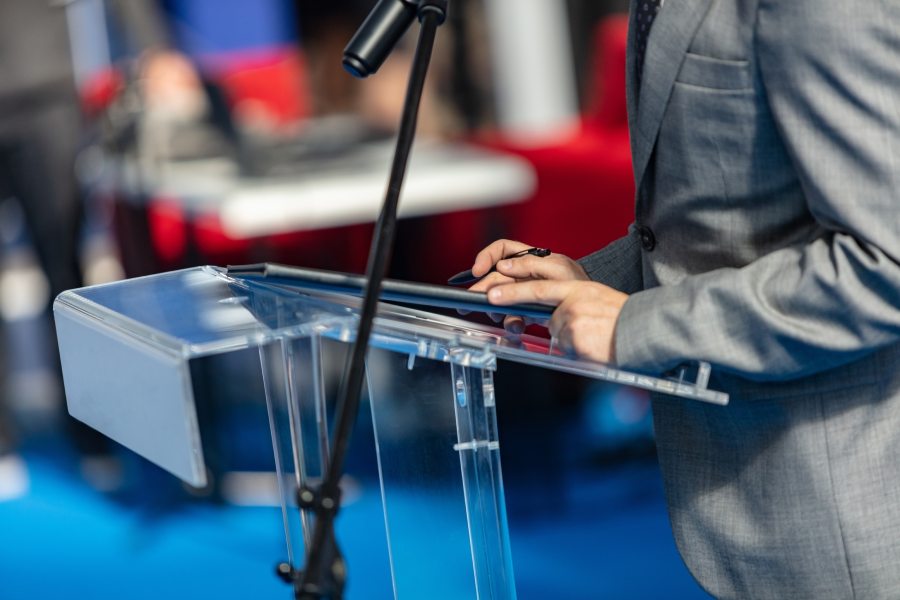 Close-up of person at a lectern with microphone during public speaking event
