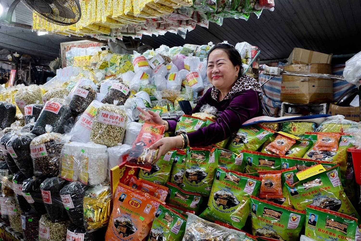 Asian individual smiles while holding bag in front of many other items at a market stand